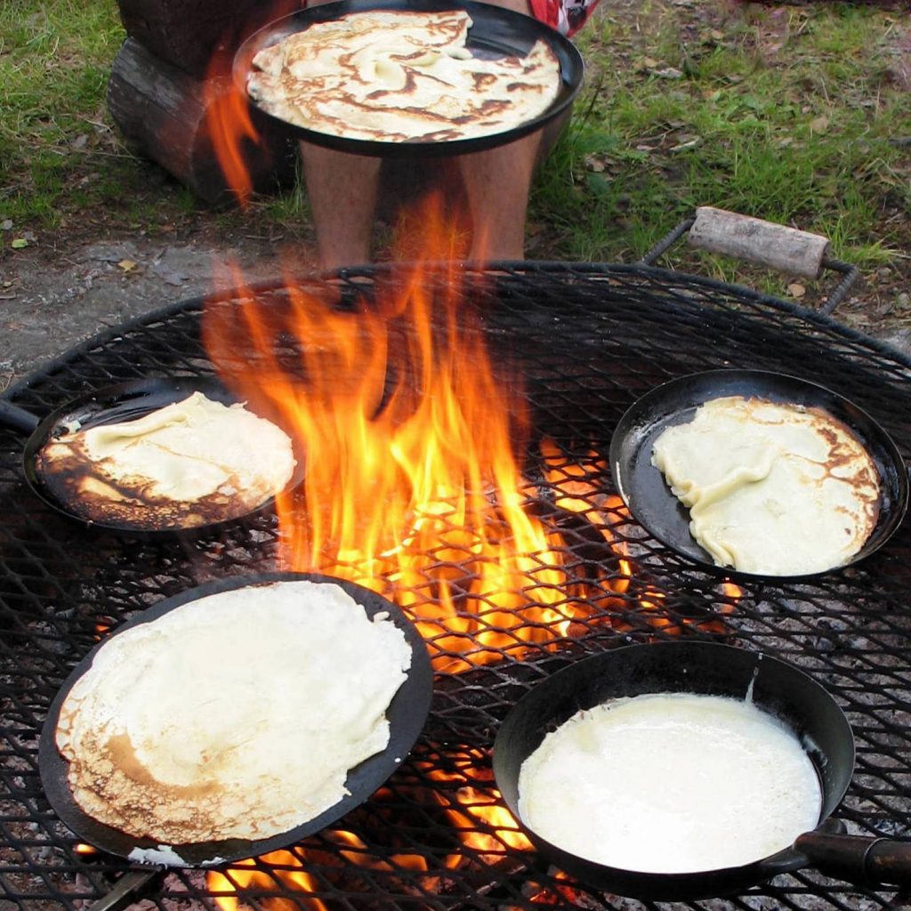 Lätyt or Pancakes being fried over a traditional nuotio or Finnish campfire.